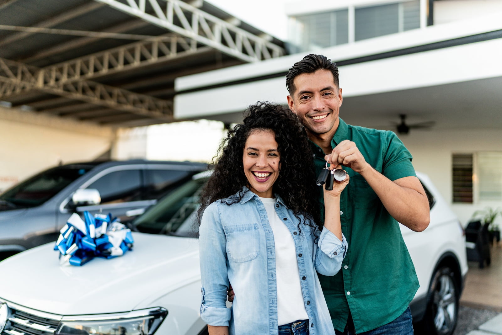 Couple holding car keys beside a new car with a bow, representing auto insurance for evolving coverage needs.