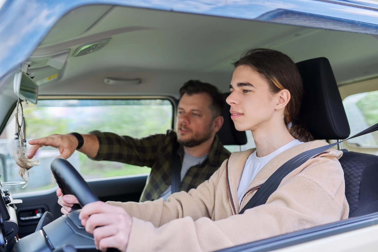 Experienced driver coaching a new driver behind the wheel, representing auto insurance protection for new drivers.