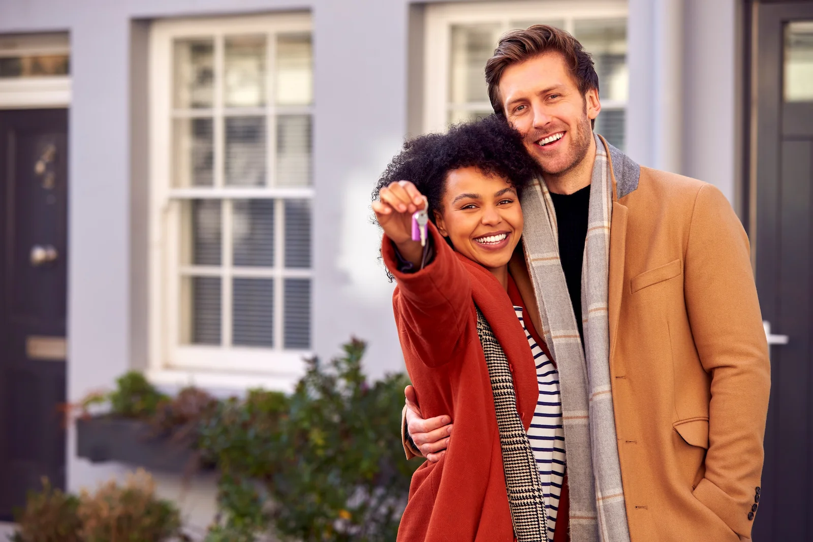 New homeowners holding house keys in front of their home, representing homeowners insurance coverage for first-time homebuyers.