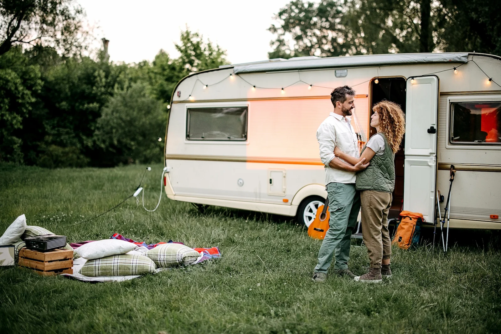 People standing beside a travel trailer at a campsite, representing recreational vehicle insurance coverage tailored to an active outdoor lifestyle.