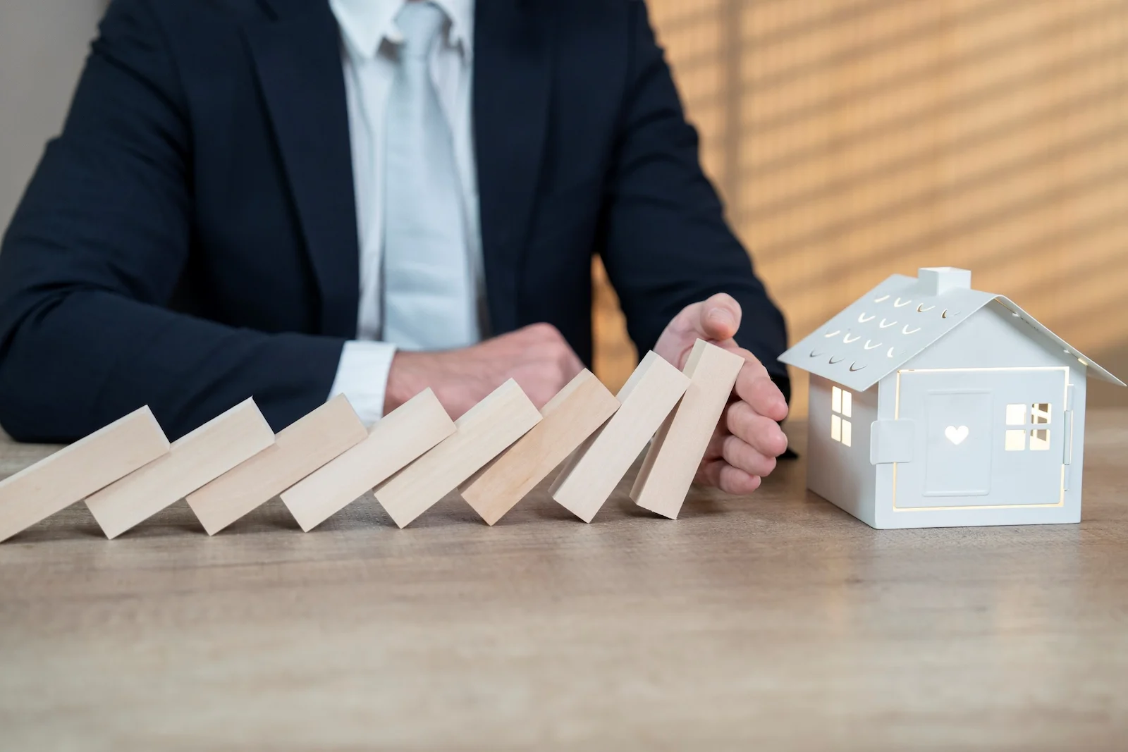 Person preventing falling wooden blocks beside a model home, representing umbrella insurance protection against personal liability claims.