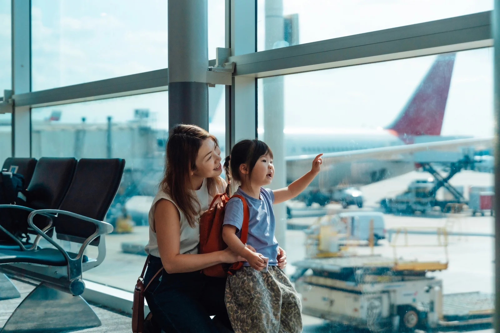 Adult traveler and child at an airport terminal overlooking an aircraft, representing worldwide umbrella insurance coverage and liability protection while traveling.