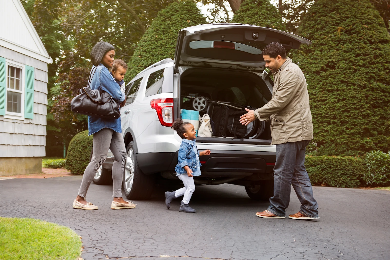 Family with two young children preparing to travel, loading belongings into a car, representing auto insurance protection.