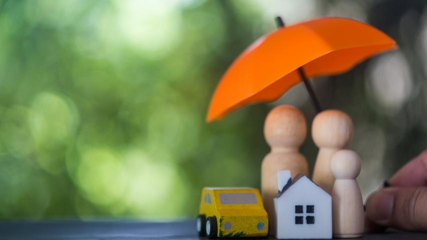 Wooden toy house, car, and family under an umbrella, representing umbrella insurance protection for assets and liability.